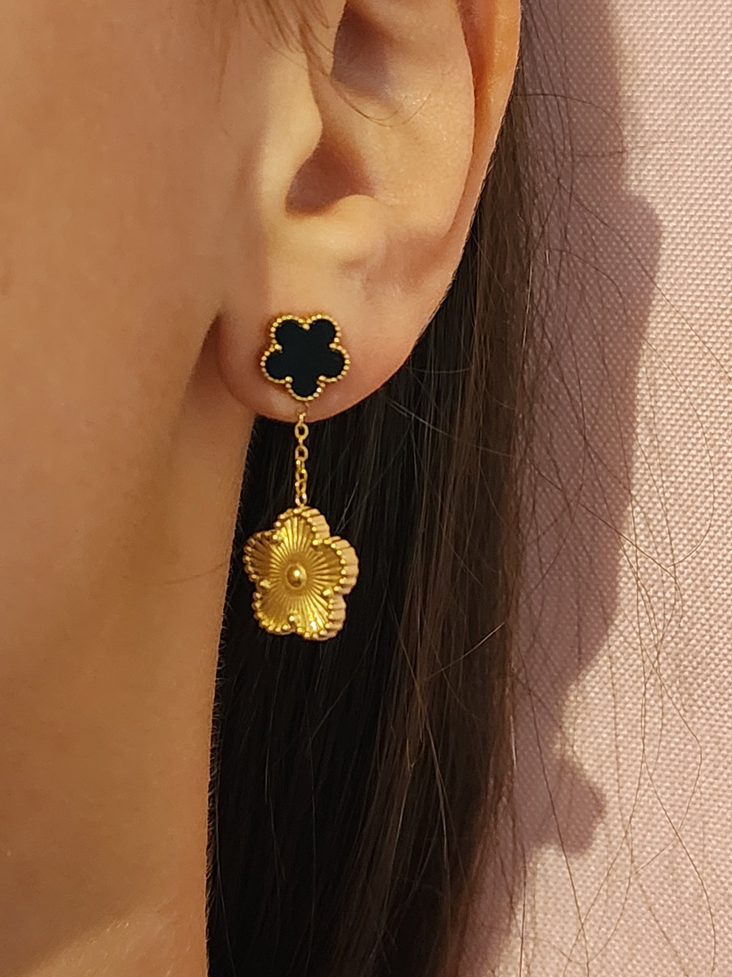 Boucles d'Oreilles Daniela en acier inoxydable doré avec fleur émaillée noire et pendentif fleur texturée, portées sur une oreille