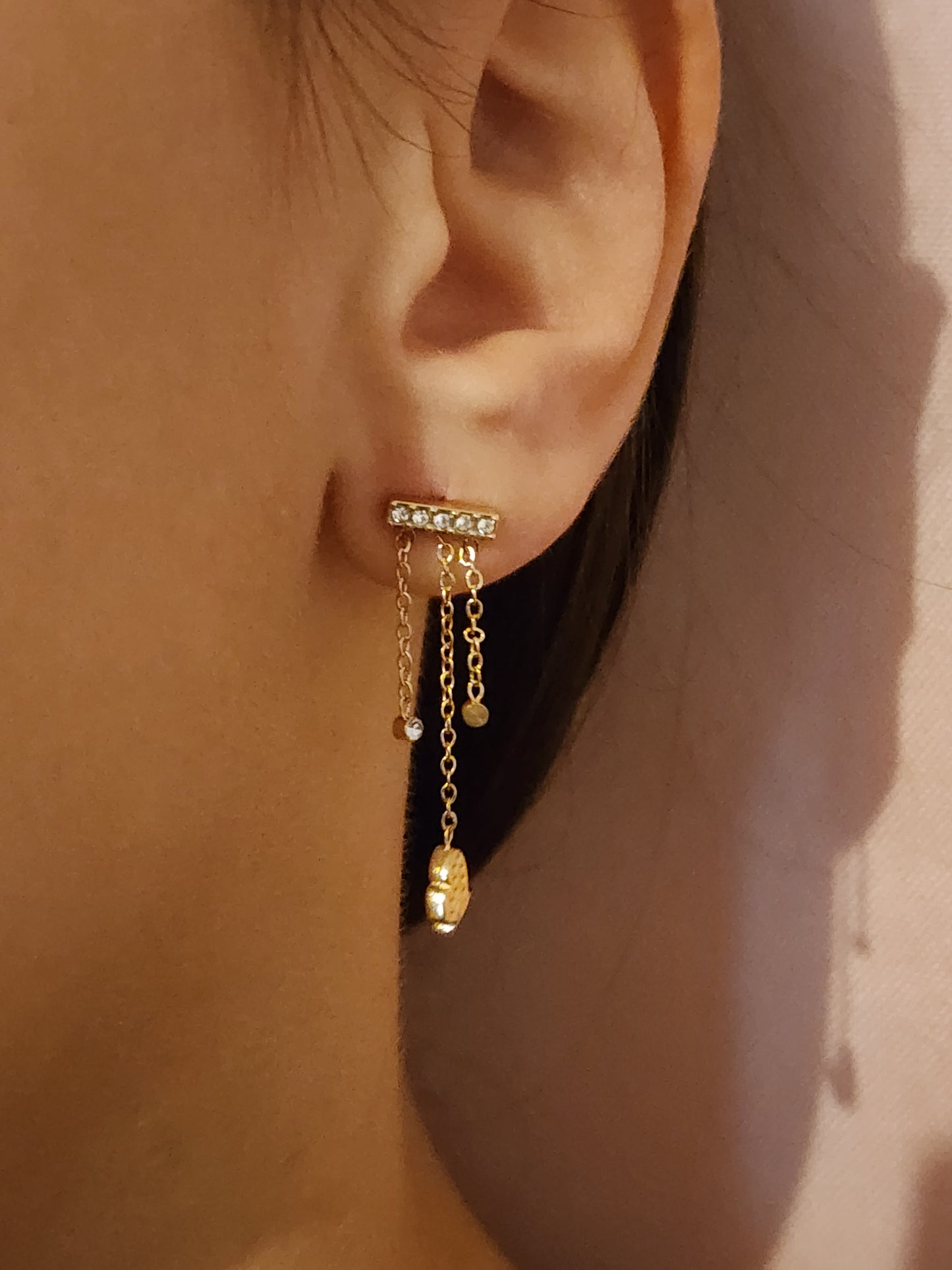 Boucles d'Oreilles Emiliana en acier inoxydable doré avec chaînes délicates et pendentif cœur, portées sur une oreille