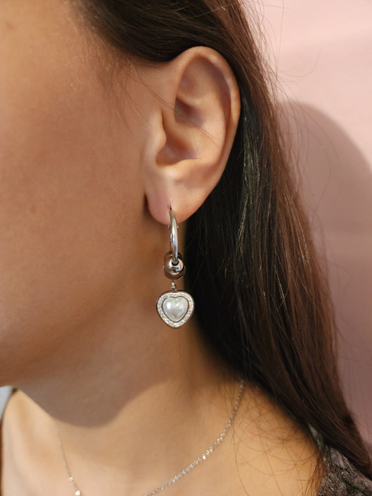 Boucles d'Oreilles Lila en acier inoxydable argenté avec pendentif cœur nacré et strass, portées sur une oreille