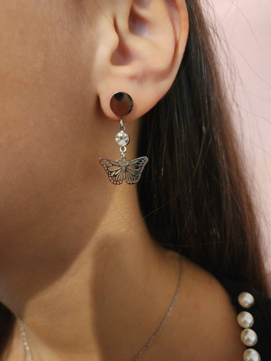Boucles d'Oreilles Paméla en acier inoxydable argenté avec design papillon élégant et strass, portées sur une oreille