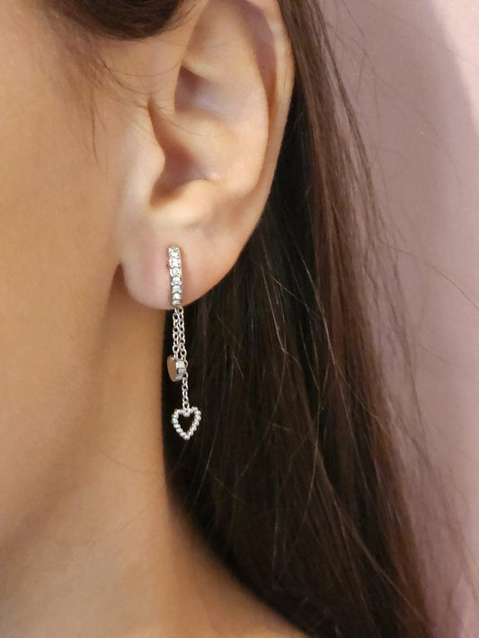 Boucles d'Oreilles Olivia en acier inoxydable argenté avec cœur ajouré et chaînes scintillantes, portées sur une oreille