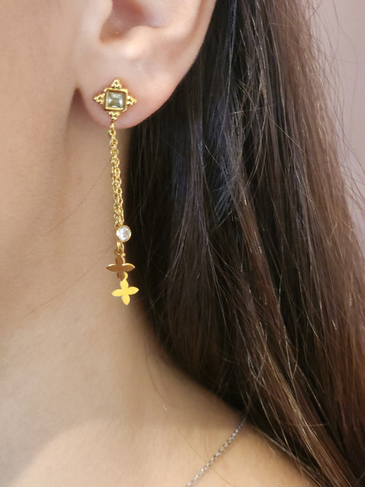 Boucles d'Oreilles Térésa en acier inoxydable doré avec chaînes délicates et pendentifs fleurs, portées sur une oreille.