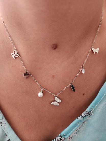 Collier Blanca en acier inoxydable argenté avec breloques papillon, fleurs, feuille, perle et strass, porté sur un cou